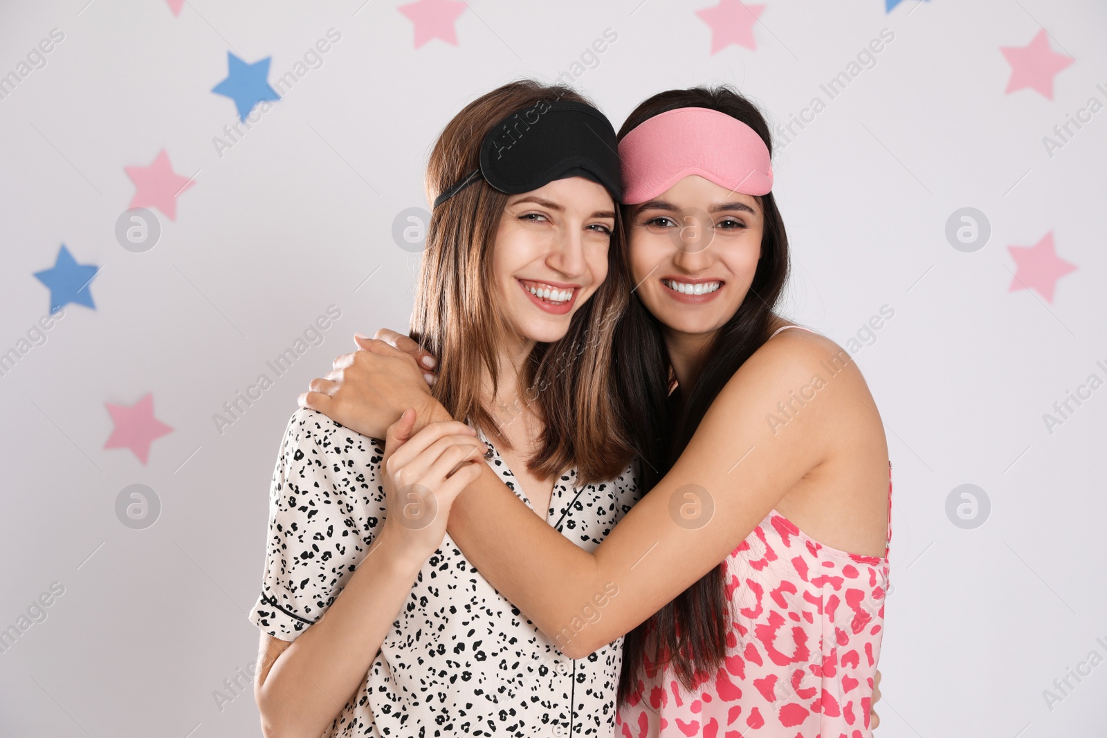 Photo of Beautiful women wearing sleeping masks on light grey background. Bedtime