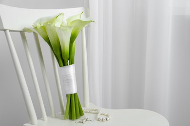 Beautiful calla lily flowers tied with ribbon and jewelry on white chair indoors