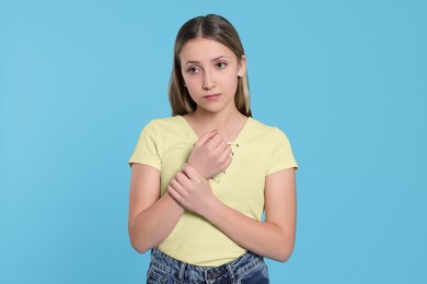 Photo of Teenage girl suffering from pain in wrist on light blue background. Arthritis symptom