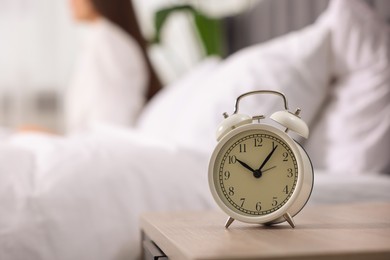 Photo of Alarm clock on nightstand. Woman awakening on bed at home, selective focus