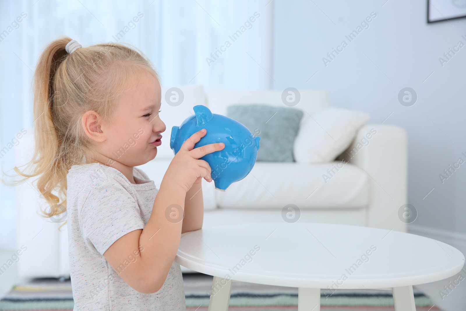 Photo of Little girl with piggy bank at home. Space for text