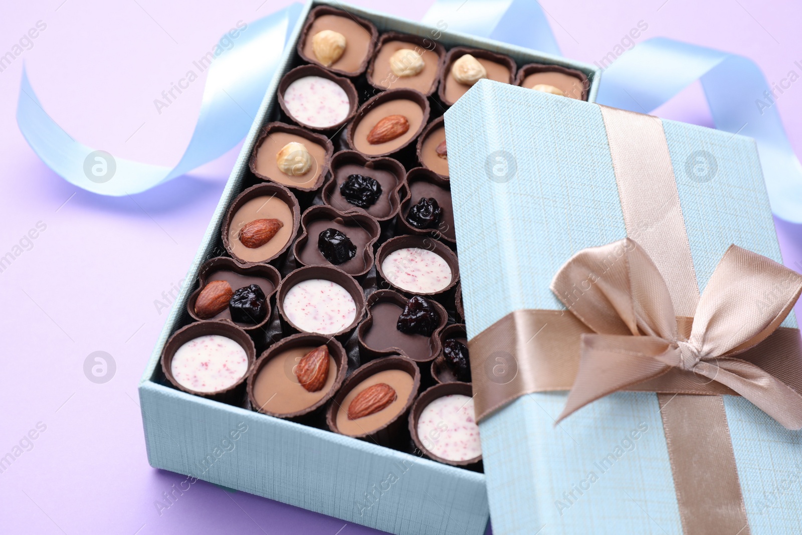 Photo of Open box of delicious chocolate candies on violet background