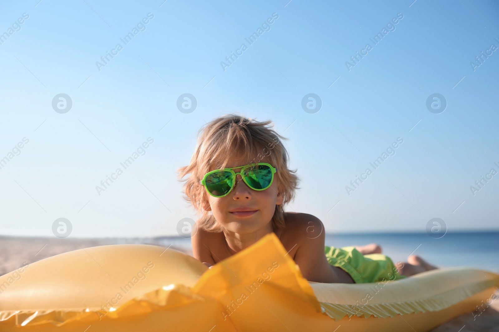 Photo of Cute little child with inflatable mattress lying at sandy beach on sunny day