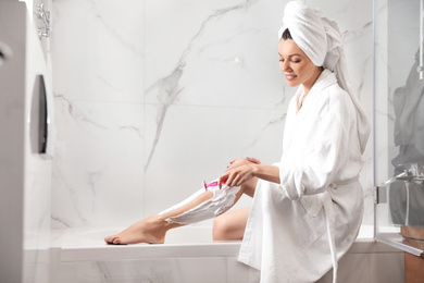 Photo of Beautiful young woman shaving legs in bathroom