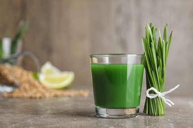 Photo of Glass of juice and fresh wheat grass on table. Space for text