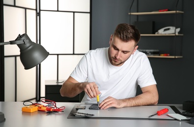 Photo of Technician repairing mobile phone at table in workshop