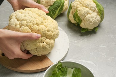 Woman with fresh cauliflower at light grey table, closeup