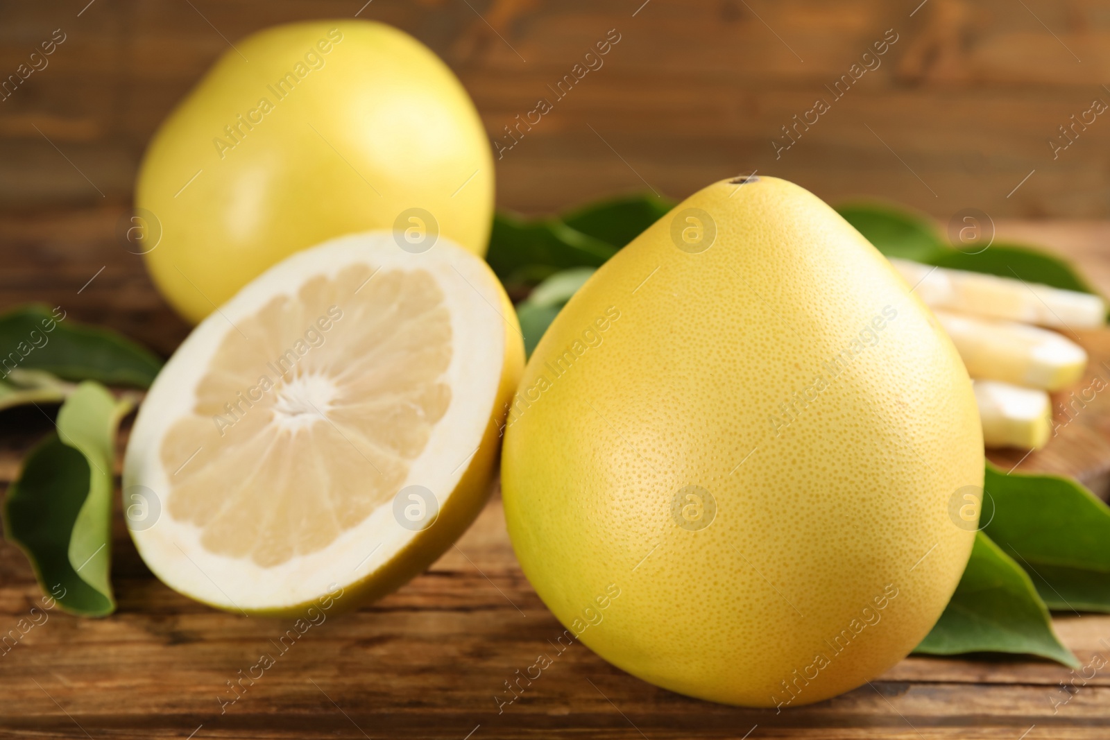 Photo of Fresh cut and whole pomelo fruits with leaves on wooden table, closeup