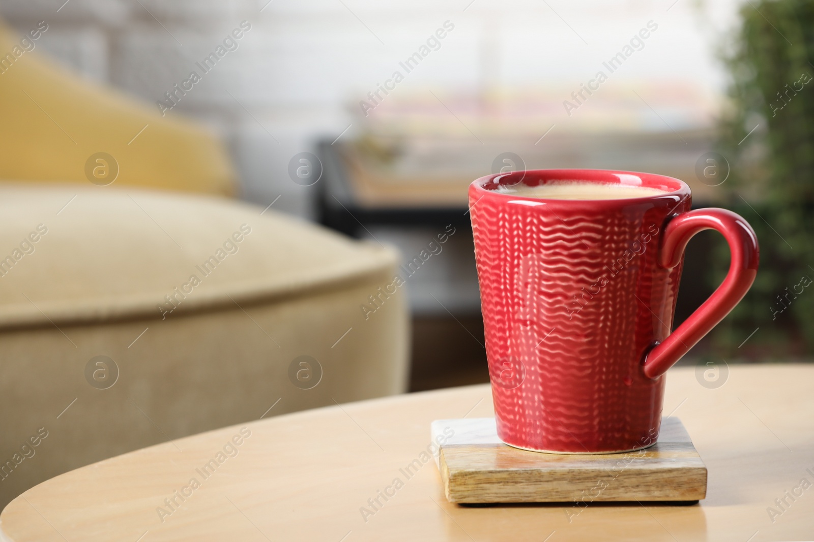 Photo of Mug of coffee with stylish cup coaster on wooden table in room. Space for text