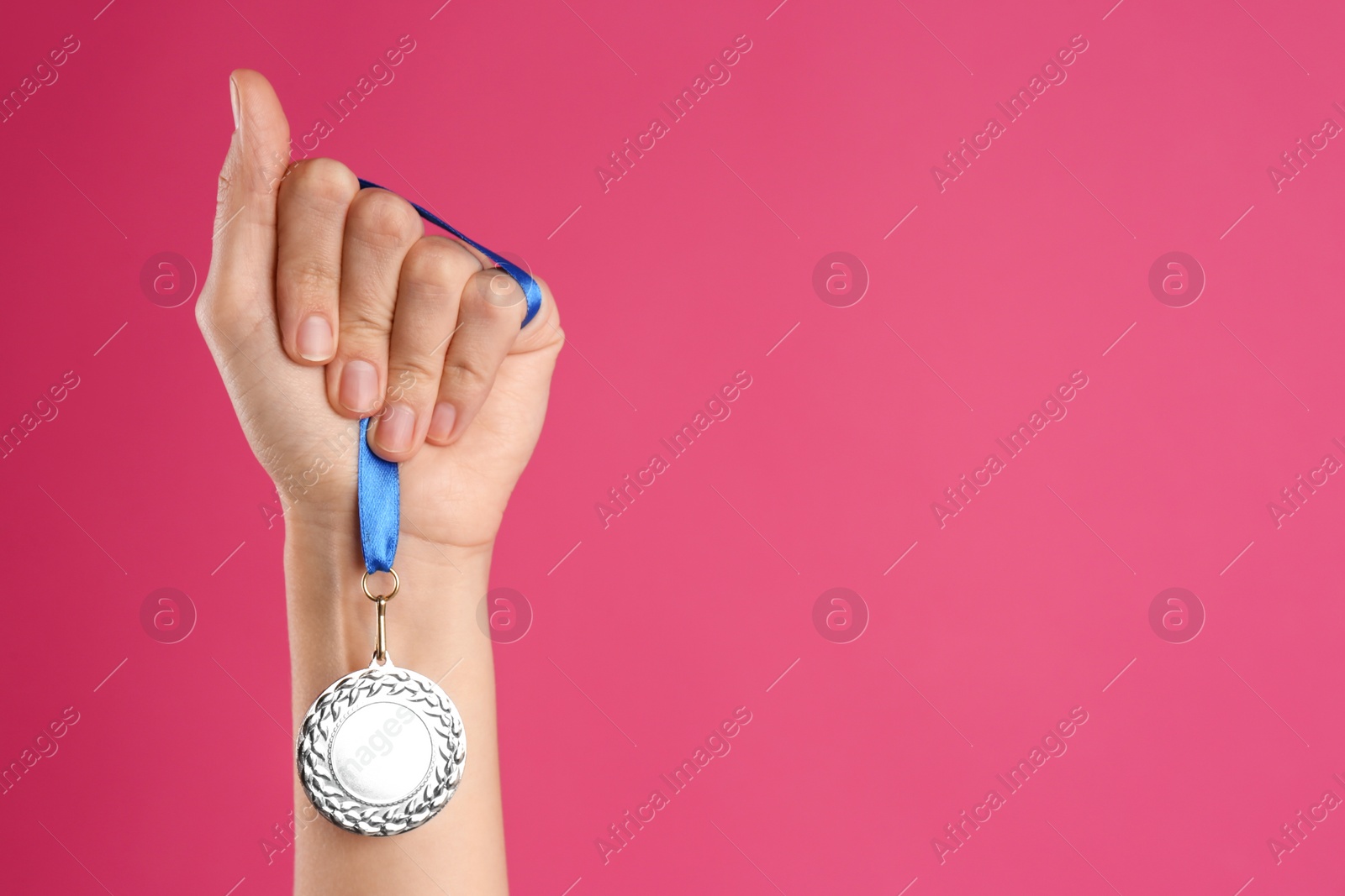 Photo of Woman holding silver medal on pink background, closeup. Space for design