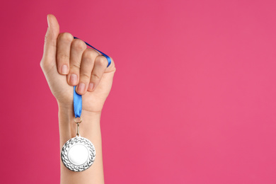 Photo of Woman holding silver medal on pink background, closeup. Space for design