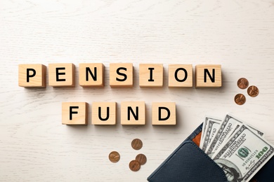 Cubes with words "PENSION FUND" and money on wooden background, flat lay