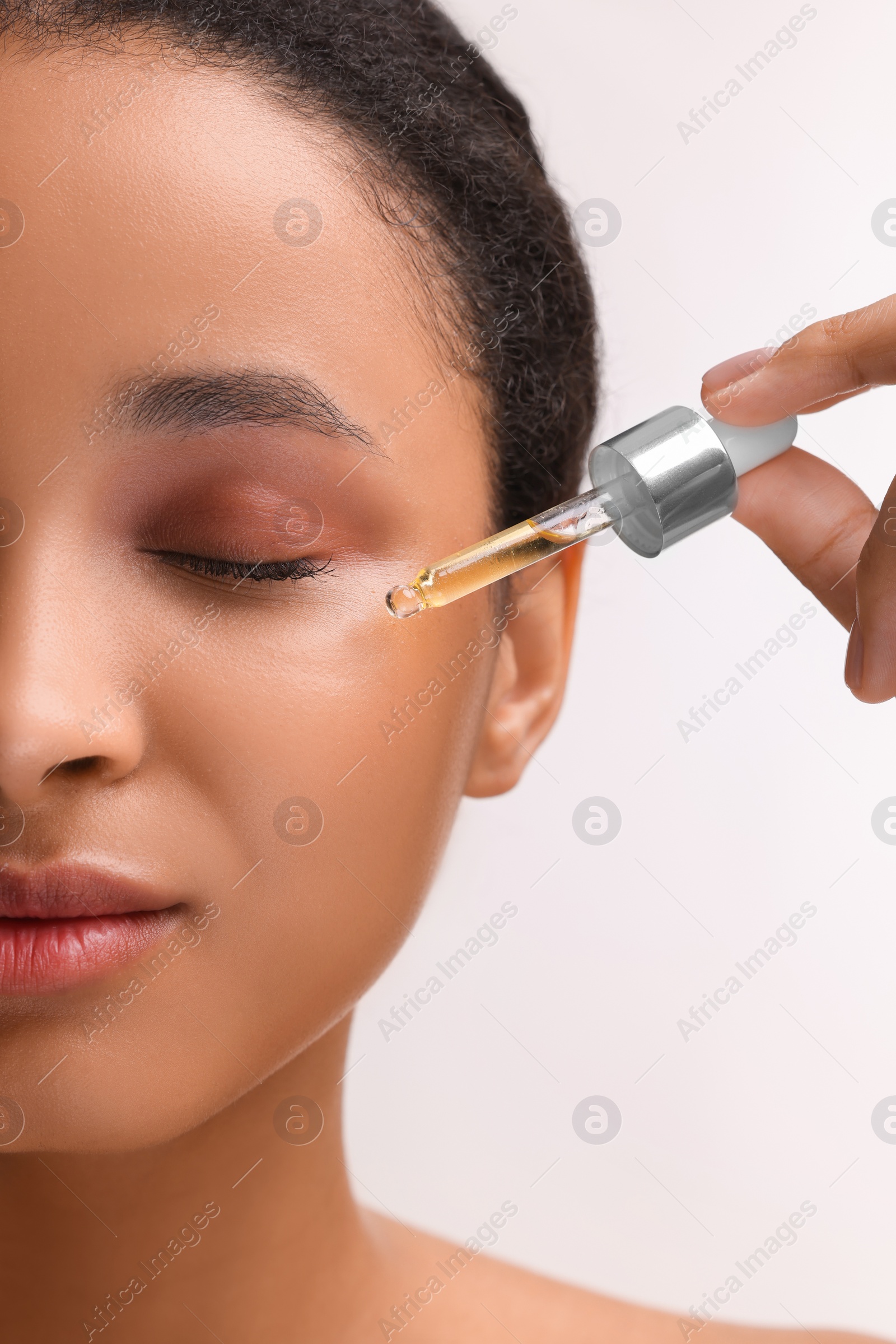 Photo of Woman applying serum onto her face on white background, closeup