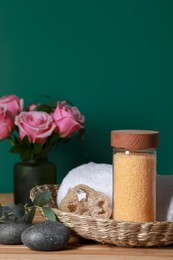 Beautiful composition with sea salt, roses and different spa products on wooden table near green wall, closeup