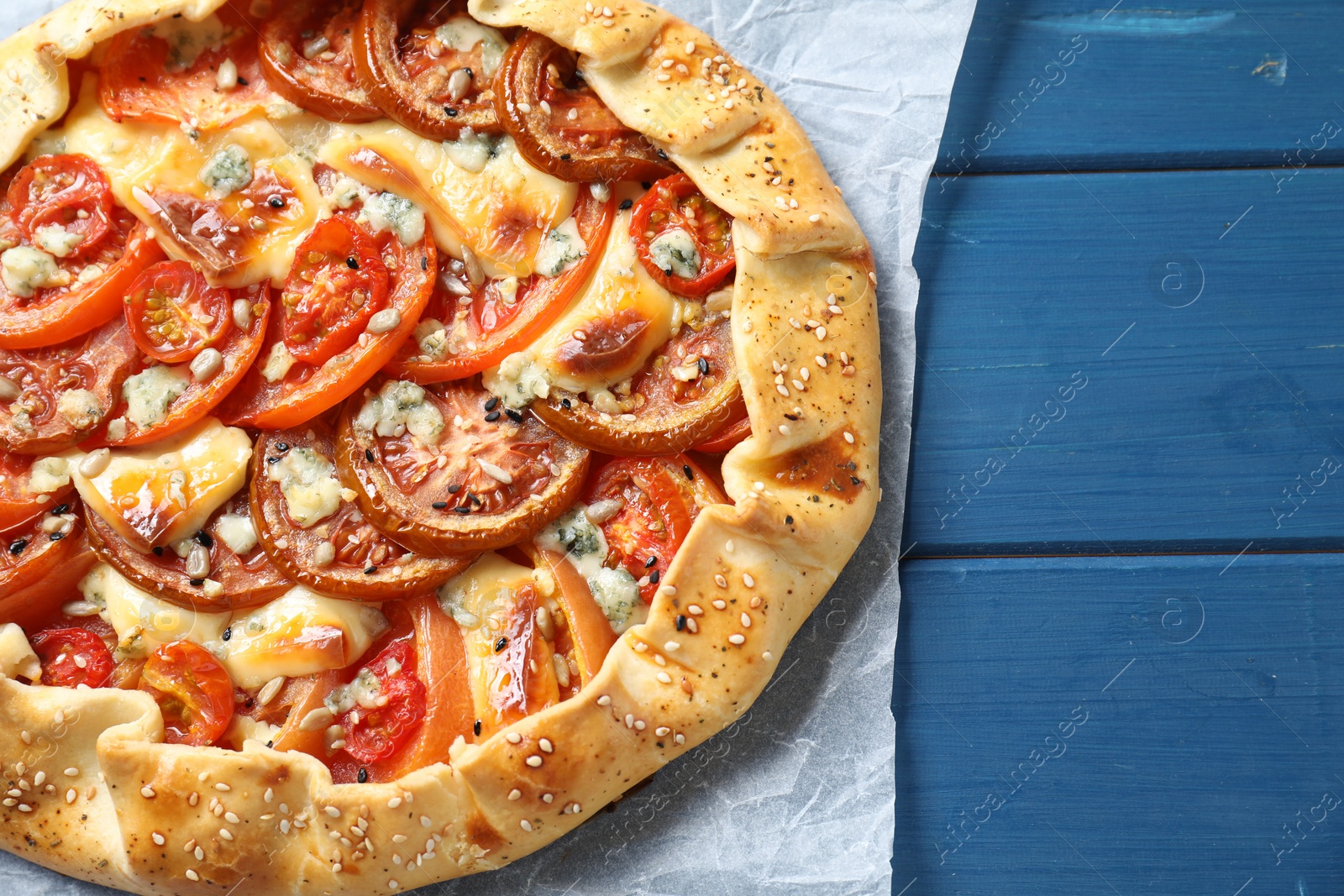 Photo of Tasty galette with tomato and cheese (Caprese galette) on blue wooden table, top view. Space for text