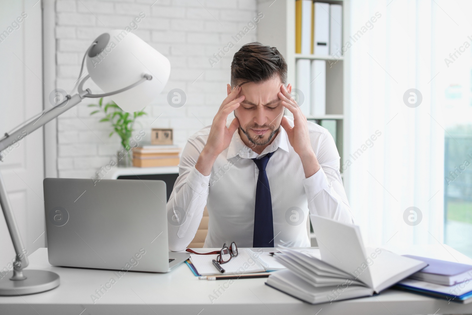 Photo of Man suffering from headache while sitting at table in office