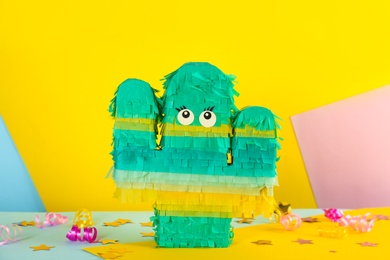Cactus shaped pinata, streamers and glitter on color background