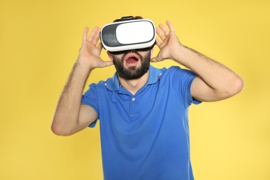 Emotional young man playing video games with virtual reality headset on color background