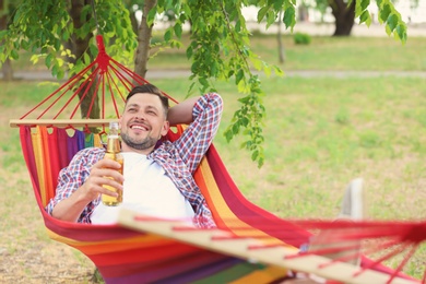 Handsome young man with bottle of beer resting in hammock outdoors