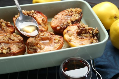 Photo of Pouring honey onto tasty baked quinces with nuts in dish at table, closeup