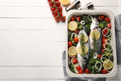 Photo of Raw fish with lemon in baking dish and vegetables on white wooden table, flat lay. Space for text