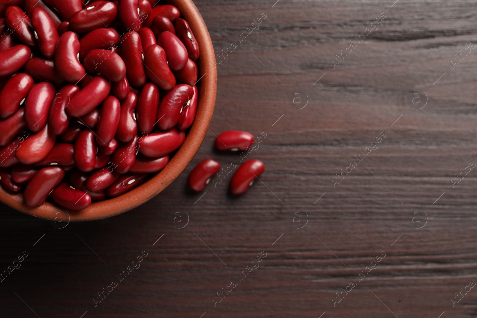 Photo of Raw red kidney beans with bowl on wooden table, flat lay. Space for text