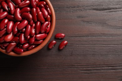 Photo of Raw red kidney beans with bowl on wooden table, flat lay. Space for text