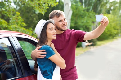 Beautiful young couple taking selfie near car