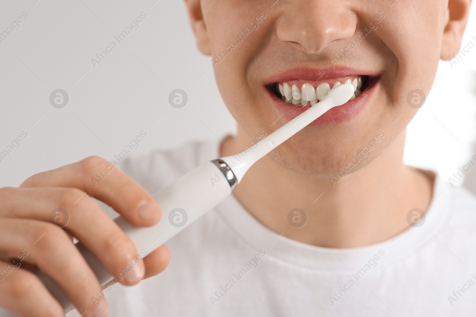 Photo of Man brushing his teeth with electric toothbrush on blurred background, closeup