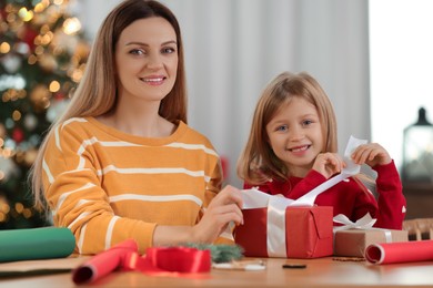 Photo of Christmas presents wrapping. Mother and her little daughter decorating gift box with ribbon at home