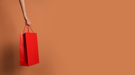 Photo of Woman holding paper shopping bag on light brown background, closeup