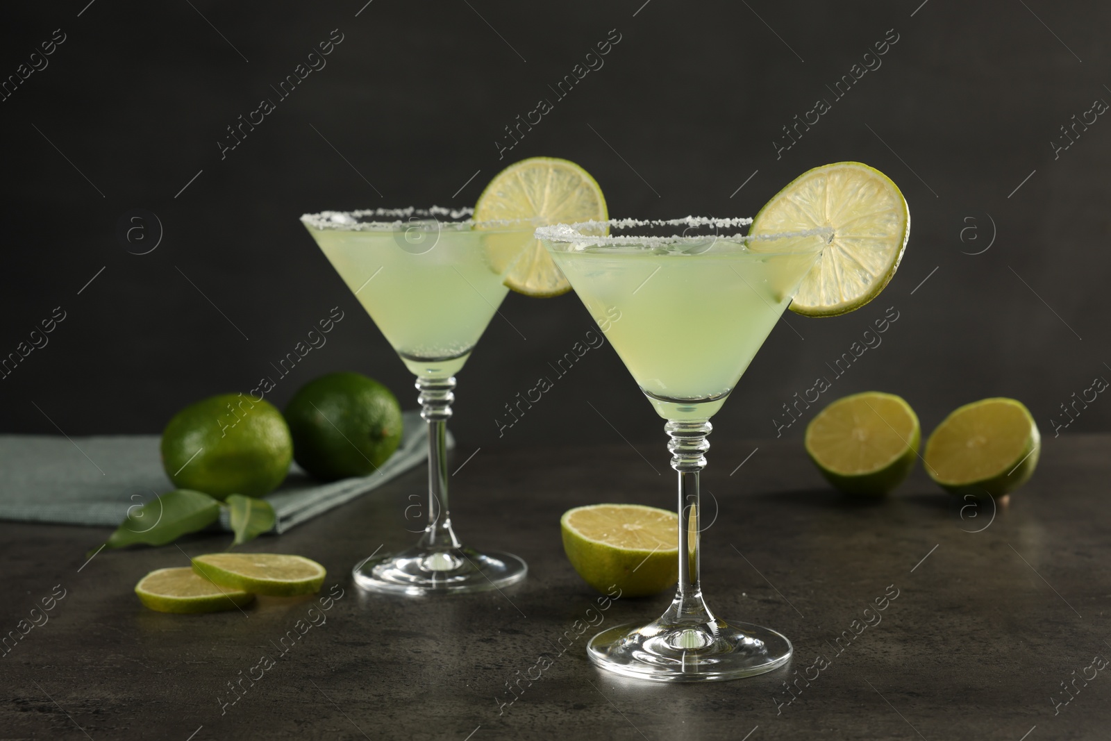 Photo of Delicious Margarita cocktail in glasses and limes on grey table