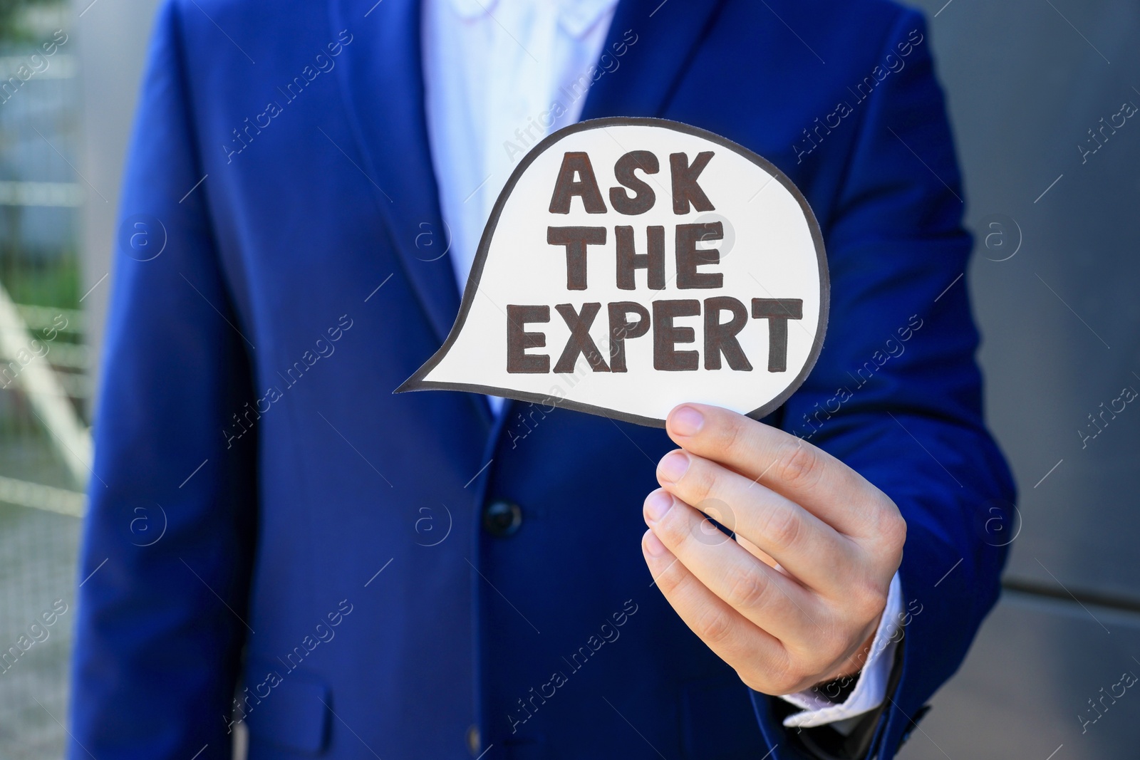 Photo of Man holding card with phrase Ask The Expert near black wall, closeup