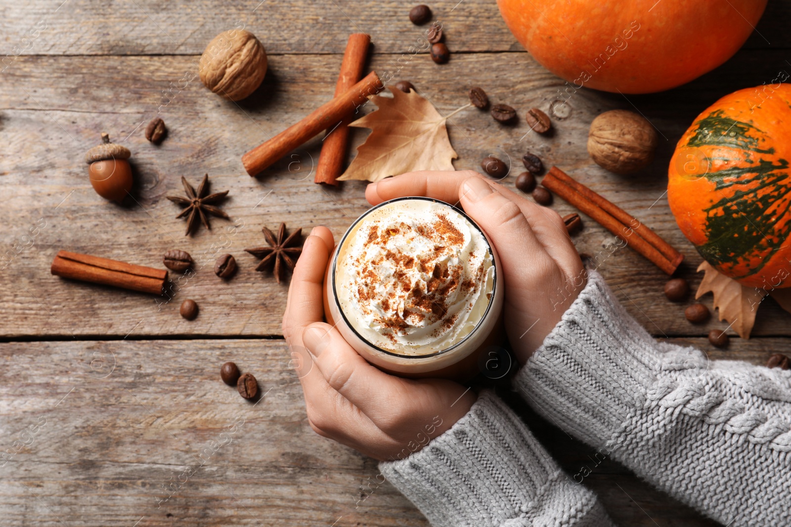 Photo of Woman holding glass of tasty pumpkin spice latte on wooden table, flat lay composition