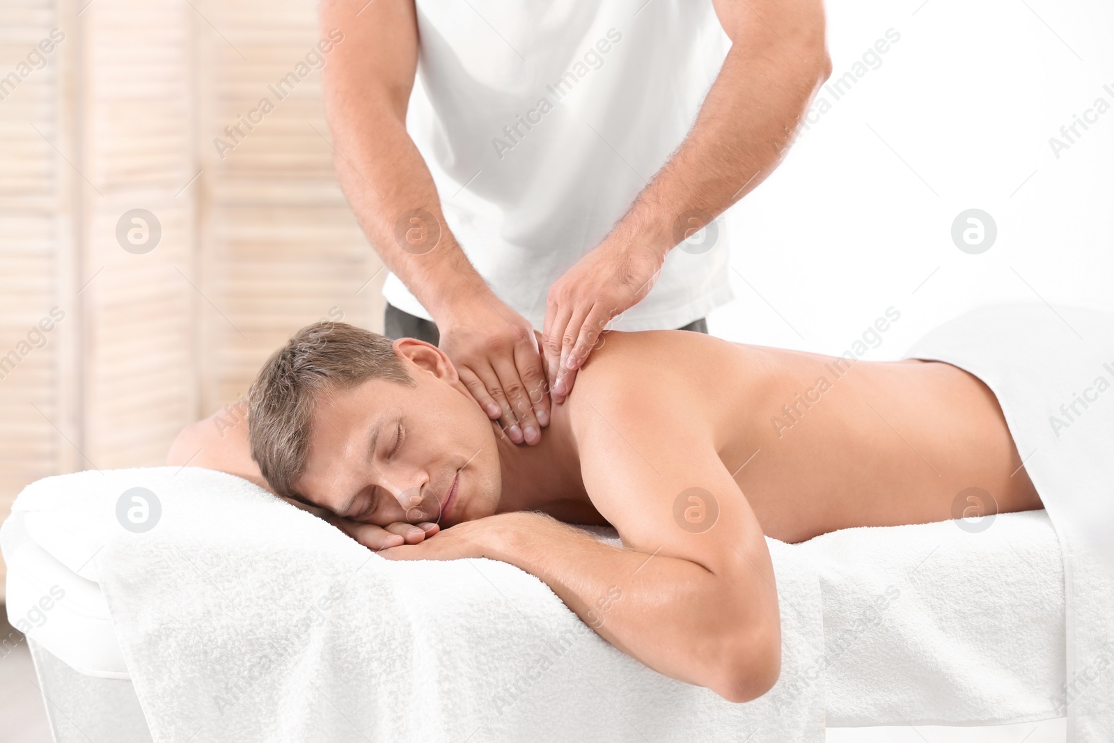 Photo of Relaxed man receiving shoulders massage in wellness center