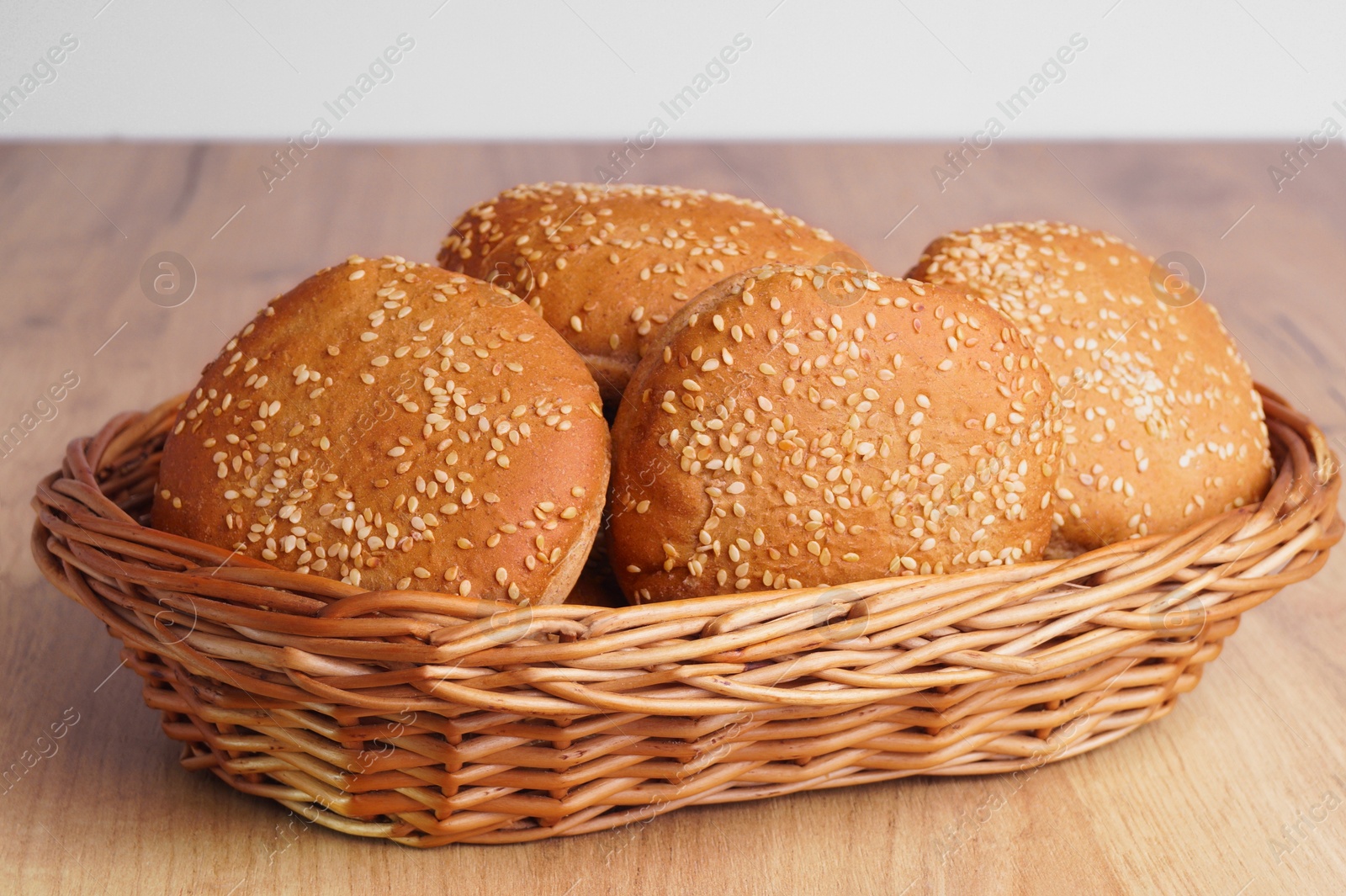 Photo of Wicker basket of fresh buns with sesame seeds on wooden table