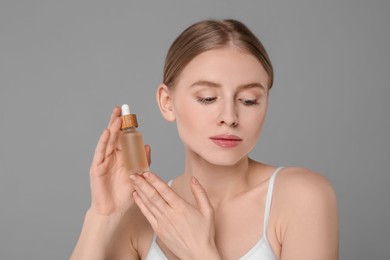 Photo of Beautiful young woman with bottle of essential oil on light grey background