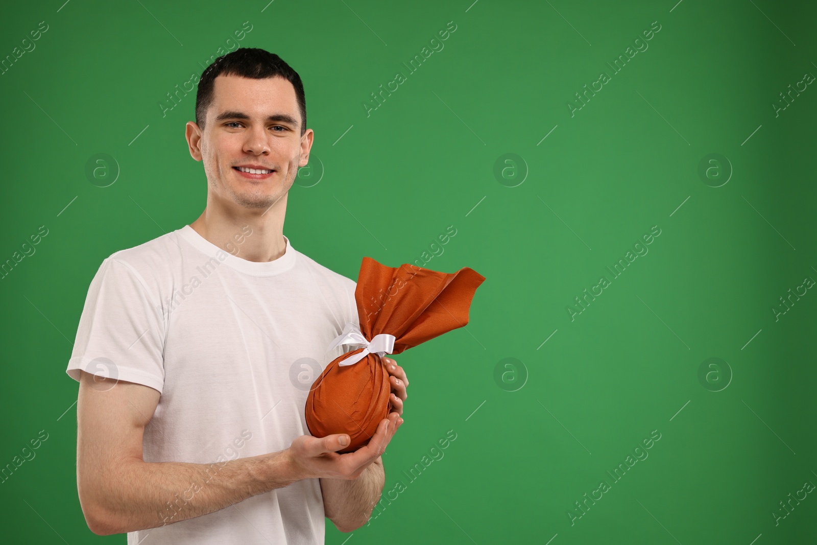 Photo of Easter celebration. Handsome young man with wrapped gift on green background. Space for text