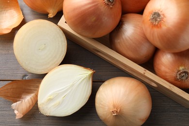 Whole and cut onions on wooden table, flat lay