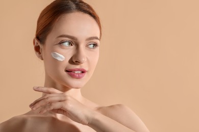 Photo of Beautiful young woman with sun protection cream on her face against beige background, space for text