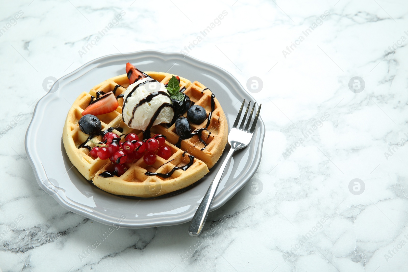 Photo of Delicious Belgian waffles with ice cream, berries and chocolate sauce on light marble table, space for text