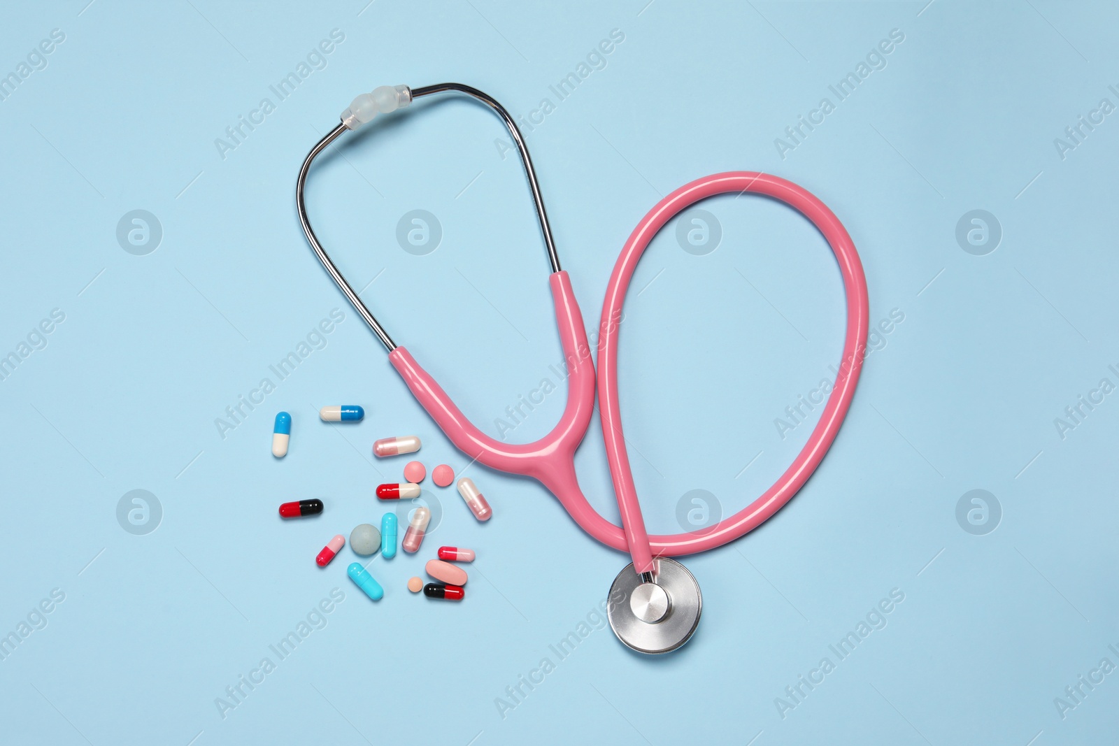 Photo of Stethoscope and pills on light blue background, top view. Medical tool