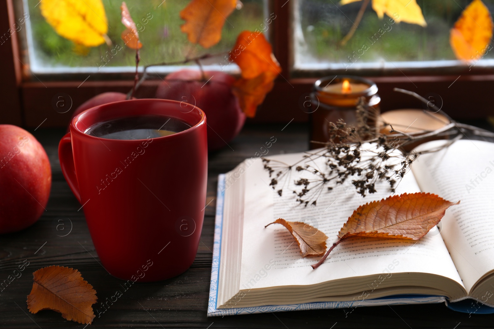 Photo of Book with dried flower as bookmark and cup of hot drink on wooden table