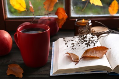 Photo of Book with dried flower as bookmark and cup of hot drink on wooden table