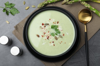 Photo of Bowl of delicious asparagus soup served on dark table, flat lay