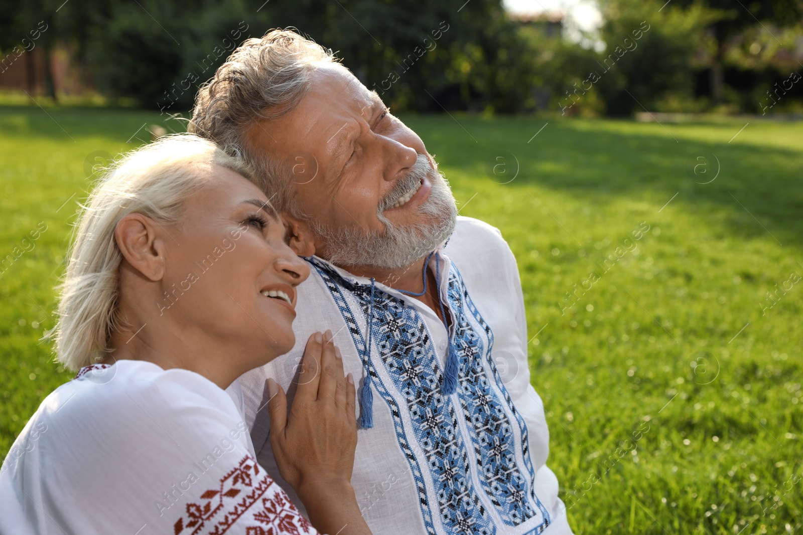 Photo of Happy mature couple in Ukrainian national clothes resting on green grass outdoors