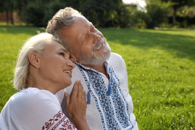 Happy mature couple in Ukrainian national clothes resting on green grass outdoors