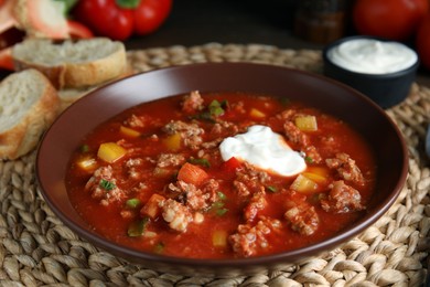 Photo of Bowl of delicious stuffed pepper soup on wicker mat, closeup