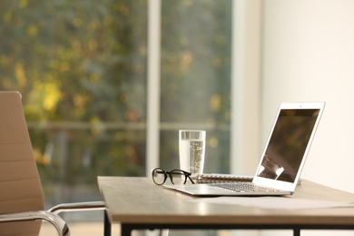 Modern laptop, notebook and glasses on table in office. Space for text