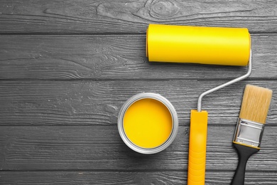 Flat lay composition with can of paint, brush and roller on grey wooden background. Space for text